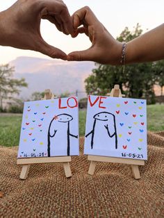 two people making a heart with their hands while standing next to each other in front of an easel