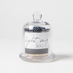 a glass jar filled with blueberries sitting on top of a white table next to a sign that says light may fire