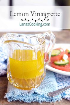 lemon vinaigrete in a glass pitcher on a blue towel next to a plate with cucumbers and watermelon