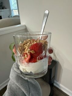 a person holding up a glass with yogurt and strawberries in it