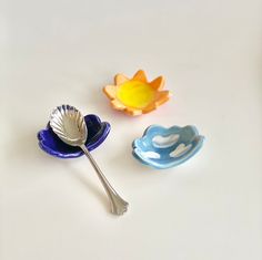 three spoons sitting next to each other on top of a white surface with a yellow flower in the middle