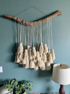 a wall hanging with tassels on it next to a lamp and potted plant