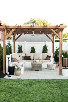 a white couch sitting under a wooden pergoline on top of a lush green field