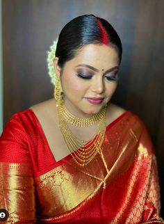 a woman in a red and gold sari with jewelry on her neck, looking down