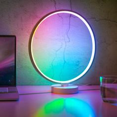 a laptop computer sitting on top of a desk next to a colorful light that looks like a circle