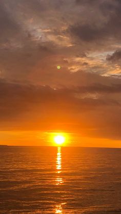 the sun is setting over the ocean on a cloudy day