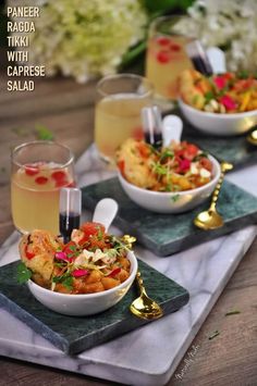 three bowls filled with food sitting on top of a marble serving tray next to two gold spoons