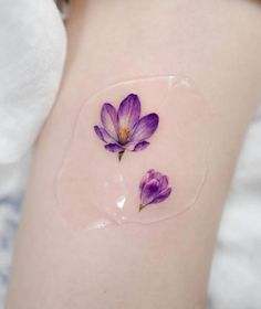 two purple flowers on the back of a woman's thigh, with water droplets around them