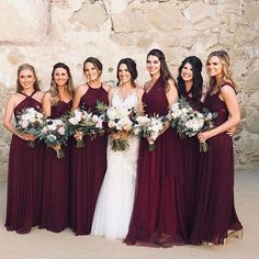 a group of women standing next to each other in front of a stone wall holding bouquets