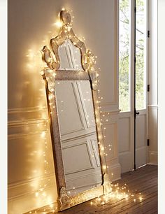 a large mirror sitting on top of a wooden floor next to a window covered in fairy lights