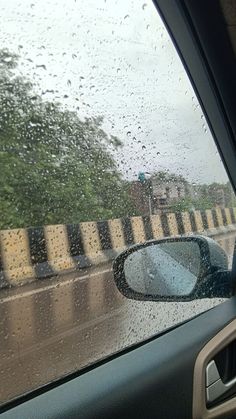 rain is falling on the windshield of a car as it drives down a road in front of a fence