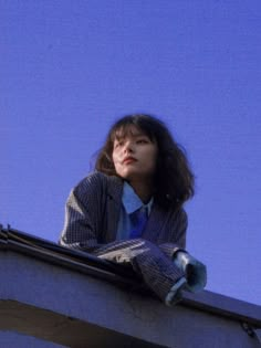 a woman sitting on top of a building next to a clock tower with her hands in her pockets