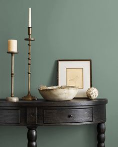 a wooden table with a bowl and two candles sitting on top of it next to a framed photograph