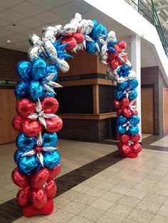 an arch made out of balloons in the middle of a lobby with stairs and tiled flooring