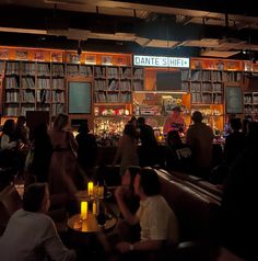 people are sitting at tables in front of bookshelves with candles on the table