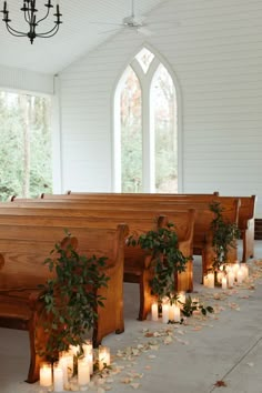 candles are lined up on the pews in front of an empty church bench with greenery