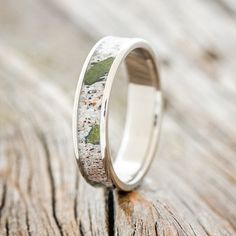 a wedding ring with moss growing on the side and white gold inlays, sitting on a wooden surface