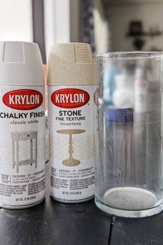 two spray paint cans sitting on top of a wooden table next to a glass cup