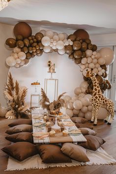 a giraffe standing next to a table filled with lots of balloons and decorations