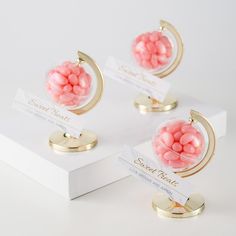 three small pink candies in a glass ball on top of a white stand next to each other