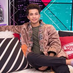 a young man sitting on top of a couch next to a large pillow and pillows