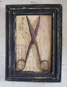 a pair of scissors sitting on top of a piece of paper in a framed frame