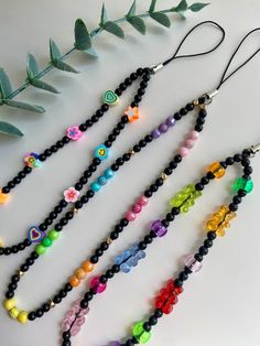 four necklaces with different colored beads and charms hanging from the strings on a white surface