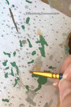 a person is using a pen to paint the paper with green and yellow designs on it