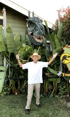 a man standing in front of a fake t - rex with his hands up and arms wide open