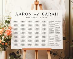 an easel with a wedding seating chart on it next to flowers and greenery