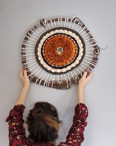 a woman is holding up a decorative plate on the wall above her head and looking down at it