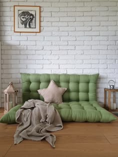 a green futon bed sitting on top of a hard wood floor next to a white brick wall