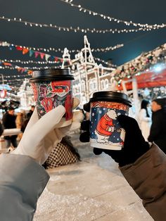 two people holding up coffee cups in front of christmas lights