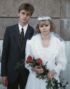 a young man and woman dressed in wedding attire standing next to each other holding roses