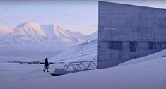 a person standing in the snow next to a large building with mountains in the background