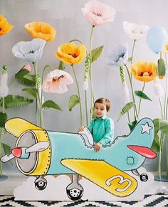 a little boy sitting on top of a toy plane in front of some paper flowers