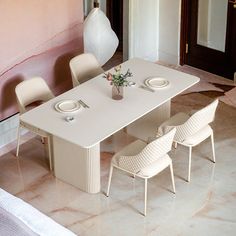 a dining table with four chairs and a vase on it in the middle of a room