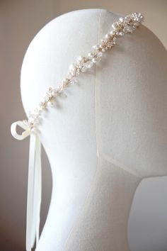 a white headband with pearls and ribbon on top of a mannequin's head