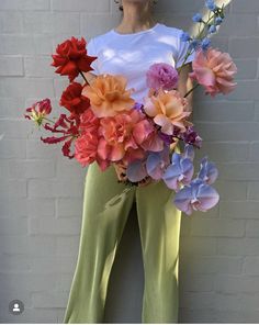 a woman holding a bouquet of flowers in front of her face and wearing green pants