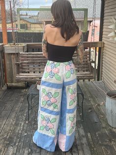 a woman standing on a porch with her back to the camera, wearing blue and pink pants