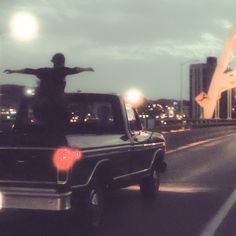 a man standing on the back of a truck in front of a bridge at night