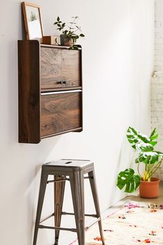 a wooden shelf above a metal stool next to a white wall with potted plants on it