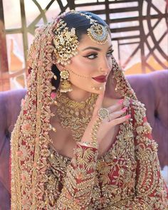 a woman in a red and gold bridal outfit with her hand on her face