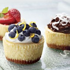 three cupcakes on a glass plate topped with whipped cream and fruit