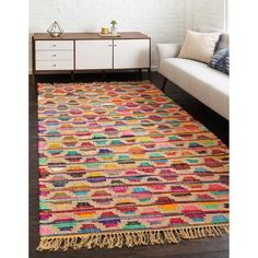 a multicolored rug with fringes on the floor in front of a white couch