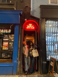 two people standing in the doorway of a restaurant with neon signs on the front door