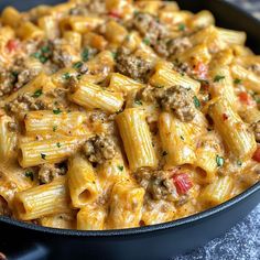 a skillet full of pasta with meat and cheese in it on a counter top