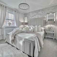 a large bed sitting in a bedroom next to a window covered in white blankets and pillows