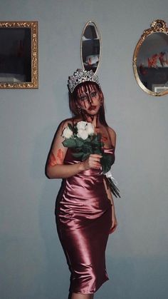 a woman in a dress holding flowers and wearing a tiara standing next to a mirror