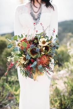 a woman wearing a white dress holding a bouquet of flowers and greenery in her hands